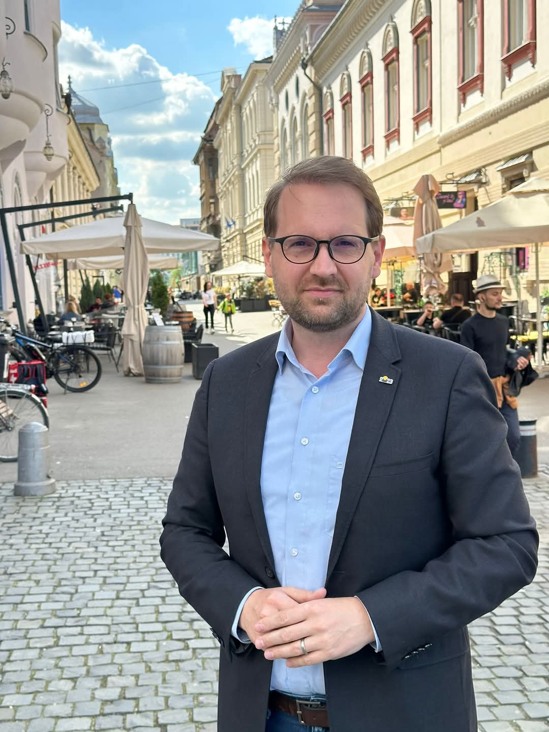 Dominic Fritz standing on a cobbled street in the historic centre of Timișoara, with cafe terraces and restored facades behind him